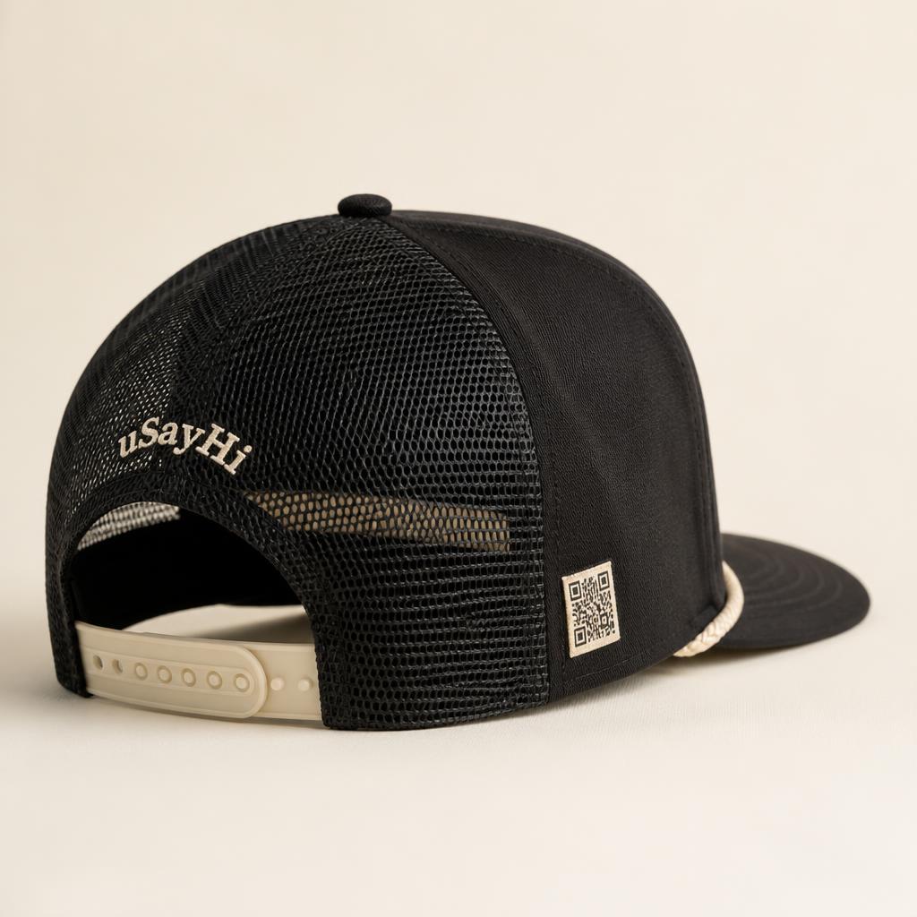 Back view of the hat showing black trucker mesh and a small arched 'uSayHi' wordmark embroidered in cream above the snapback